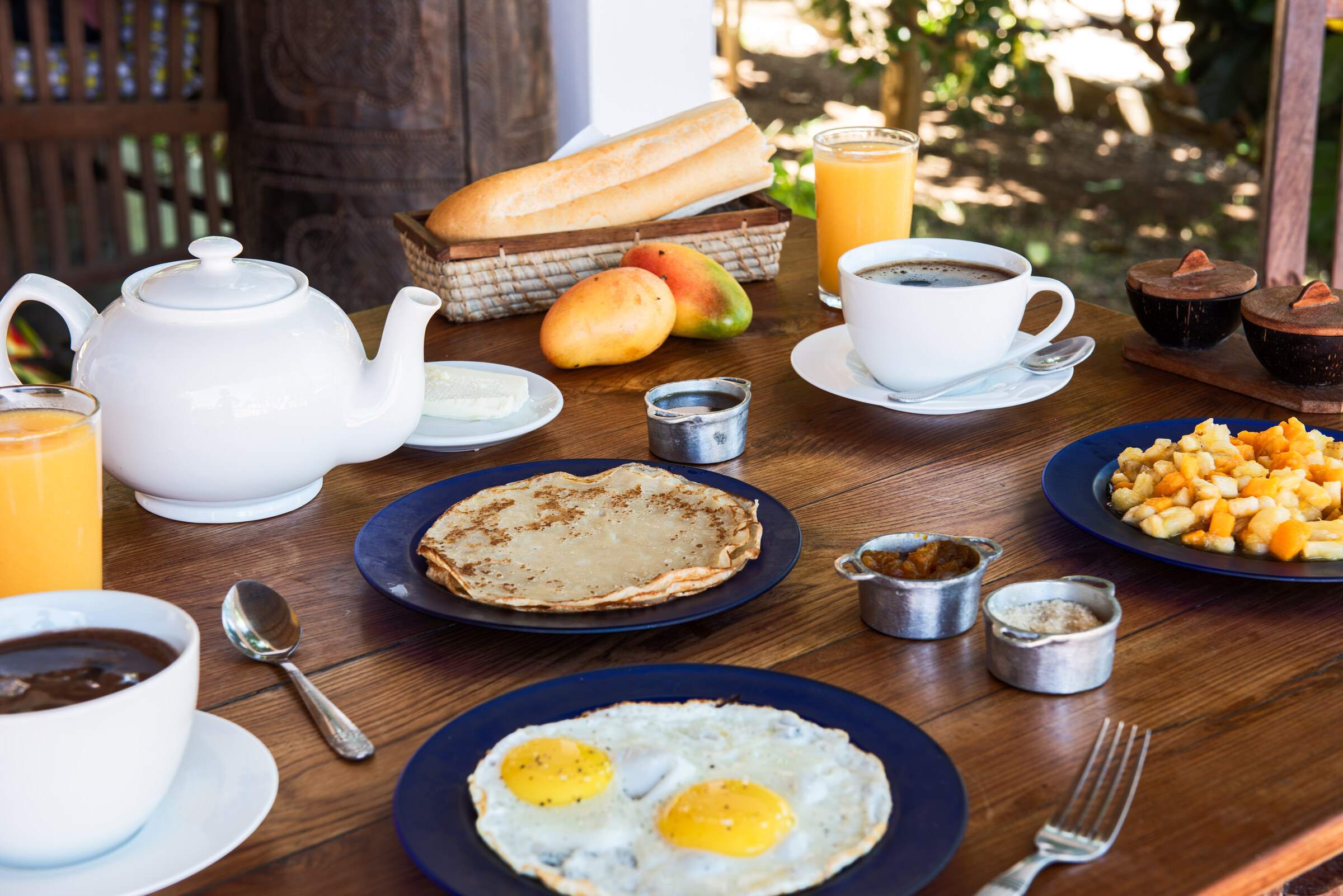 Petit-déjeuner servi : crêpes, œufs au plat, fruits frais, jus et thé